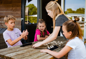 Kinderen spelen een bordspel buiten een Safarilodge tent op Camping de Noetselerberg, Nederland, zomerdag.