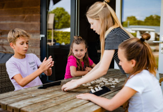 Bambini giocano a un gioco da tavolo fuori da una tenda Safarilodge al Camping Noetselerberg, Paesi Bassi.