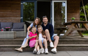 Familie sidder smilende foran deres Safarilodge-telt på Camping de Noetselerberg i Holland.