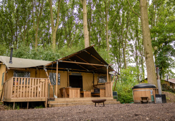 Safari tent at Glamphuys, Buitengoed Ruysbos in the Netherlands, set amidst tall trees with a cozy deck.
