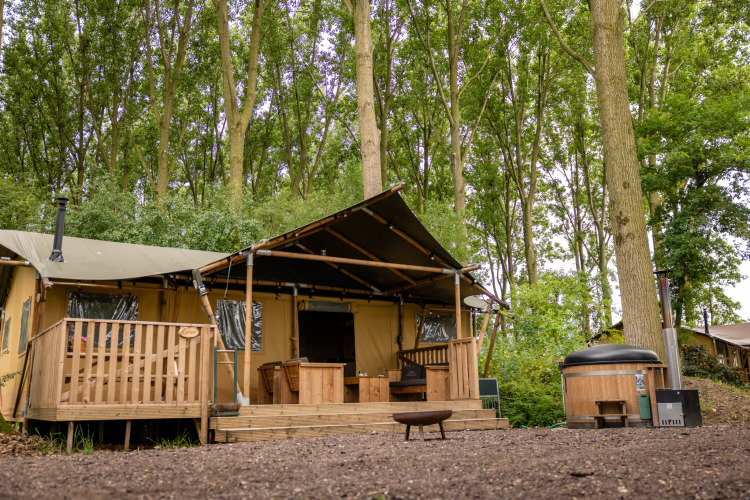 Safari tent at Glamphuys, Buitengoed Ruysbos in the Netherlands, set amidst tall trees with a cozy deck.