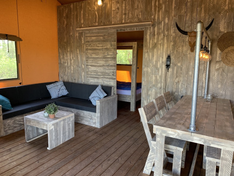 Interieur van een safaritent bij Buitengoed Ruysbos met houten meubels, zithoek en eettafel.