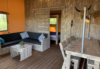 Interno di una tenda safari a Buitengoed Ruysbos con arredi rustici in legno, area lounge e pranzo.