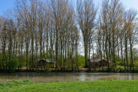 Vista a través del río hacia tiendas safari en Glamphuys, Buitengoed Ruysbos, Países Bajos, en un día soleado.