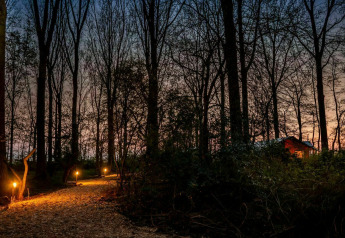 Aftensti oplyst af fakler fører gennem en skov til et glamping telt i Buitengoed Ruysbos, Holland.