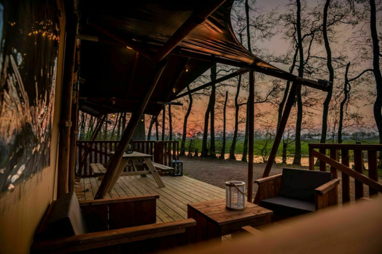 Safari tent Glamphuys at Buitengoed Ruysbos in the Netherlands, sunset view from a furnished outdoor deck.