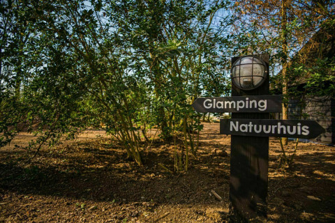 Señal en Buitengoed Ruysbos, Países Bajos, indicando glamping y casa de la naturaleza entre árboles.