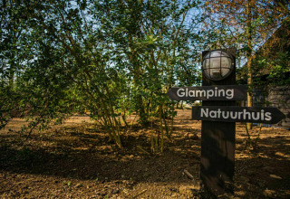 Skilt ved Buitengoed Ruysbos i Holland viser vej til glamping og naturhus, omgivet af træer.