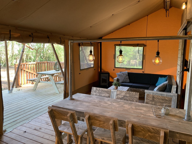 Interior of Glamphuys safari tent at Buitengoed Ruysbos, Netherlands, with wooden furniture and outdoor deck.