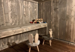Kleiner Holztisch und Stühle mit Hasenohren in rustikalem Holzraum, Spielzeug auf dem Tisch.