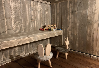 Kleine houten tafel en stoeltjes met konijnenoren in een landelijke hut, speelgoed op de tafel.