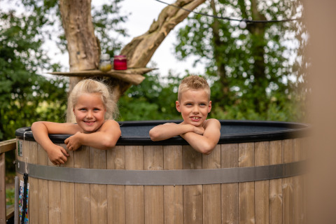 Dos niños sonrientes en un jacuzzi junto a la tienda Glamphuys en Buitengoed Ruysbos, Países Bajos.