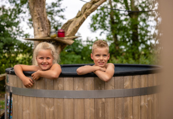 Twee kinderen glimlachen in een hottub bij Glamphuys safaritent op Buitengoed Ruysbos, Nederland.