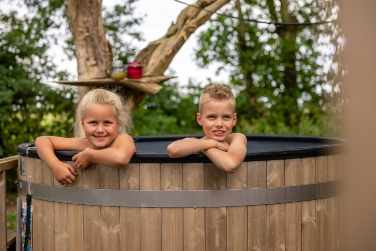 Two smiling children in a hot tub at Glamphuys safari tent at Buitengoed Ruysbos in the Netherlands.