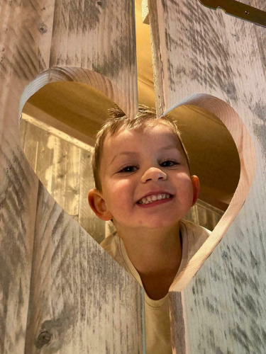 A smiling child looks through a heart-shaped hole in wood at Glamphuys, Buitengoed Ruysbos, Netherlands.