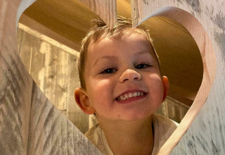 Een lachend kind kijkt door een hartvormig gat in hout bij Glamphuys, Buitengoed Ruysbos, Nederland.