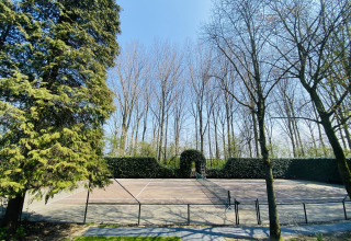 Tennis court at a glamping accommodation, surrounded by tall trees on a bright, sunny day.