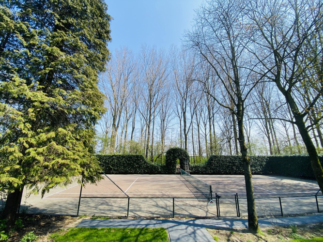 Tennis court at a glamping accommodation, surrounded by tall trees on a bright, sunny day.