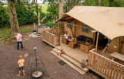 Familie slapper af og leger udenfor et luksustelt med træterrasse ved Glamphuys Ultra Wellness i Holland.