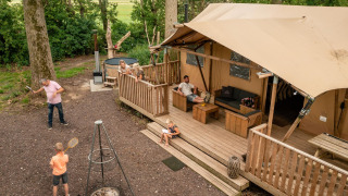 Family relaxing and playing outdoors beside a safari tent at Glamphuys Ultra Wellness in the Netherlands.