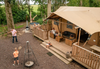 Familie slapper af og leger udenfor et luksustelt med træterrasse ved Glamphuys Ultra Wellness i Holland.