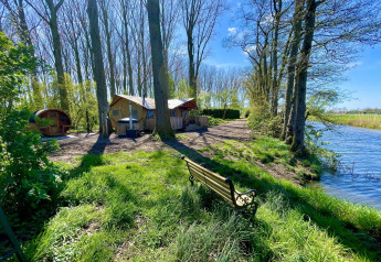 Tienda safari Glamphuys Ultra Wellness junto al agua en Buitengoed Ruysbos, Países Bajos, con árboles y sol.