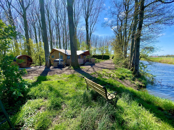Safari tent Glamphuys Ultra Wellness by the water at Buitengoed Ruysbos, Netherlands, with trees and sunlight.