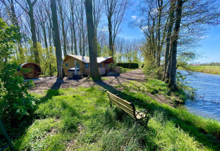 Tienda safari Glamphuys Ultra Wellness junto al agua en Buitengoed Ruysbos, Países Bajos, con árboles y sol.