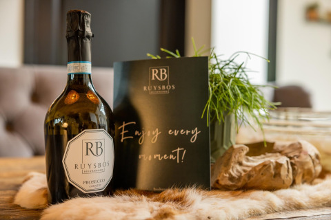 Botella de Ruysbos Prosecco y tarjeta sobre la mesa dentro de la tienda safari Glamphuys Ultra Wellness en Buitengoed Ruysbos.