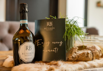 Botella de Ruysbos Prosecco y tarjeta sobre la mesa dentro de la tienda safari Glamphuys Ultra Wellness en Buitengoed Ruysbos.
