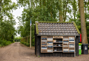 Pequeña caseta de madera con información junto a un camino de tierra y árboles en Buitengoed Ruysbos, Países Bajos.