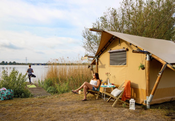 To kvinder slapper af ved en safaritelt ved søen på Marina Parcs Almere, Holland, omgivet af natur.