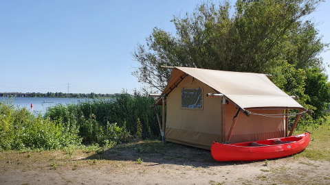Tienda safari en Marina Parcs Almere, Países Bajos, junto al lago y con una canoa roja frente a la tienda.