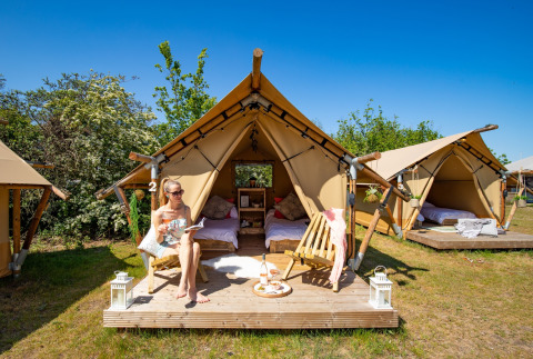 Mujer relajándose frente a tiendas safari en Marina Parcs Almere, Países Bajos, en un día soleado.