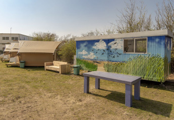 Safari-telt og farverigt malet skur ved Marina Parcs Almere i Holland, med træbænk og bord udenfor.