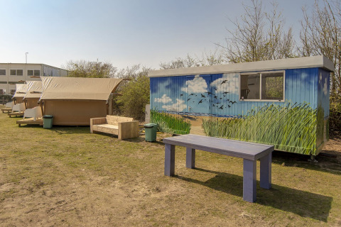 Safari-telt og farverigt malet skur ved Marina Parcs Almere i Holland, med træbænk og bord udenfor.