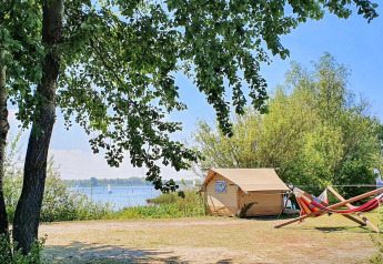 Safari-telt ved Marina Parcs Almere i Holland med udsigt over søen, hængekøjer og grønne træer.