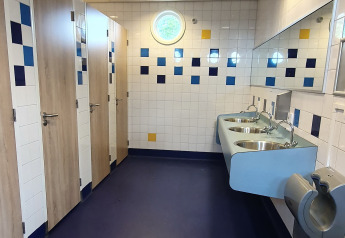 Et moderne badeværelse på et glampingsted med blå gulv, tre toiletbåse, håndvaske og spejl.