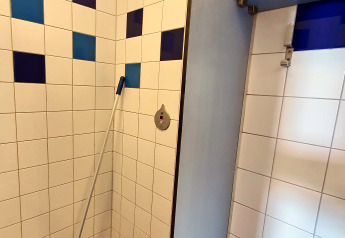 Eine Ecke eines Badezimmers mit bunten Fliesen und einem Wischmopp, aufgenommen in einer Glamping-Unterkunft.