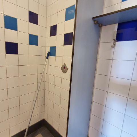 Esquina de baño con azulejos azules y morados y un trapeador, tomada en un alojamiento glamping.