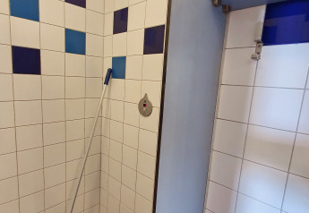 Angolo bagno con piastrelle blu e viola e uno spazzolone, fotografato in un alloggio glamping.