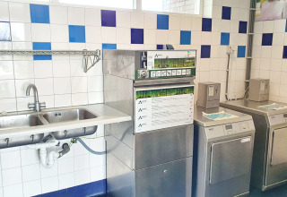 Buanderie d’un site de glamping avec lave-linge, sèche-linge et évier double en inox.