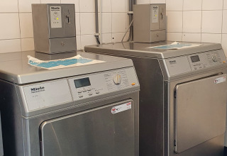 Two professional Miele washing machines and dryers in a glamping laundry room with white tiled walls.
