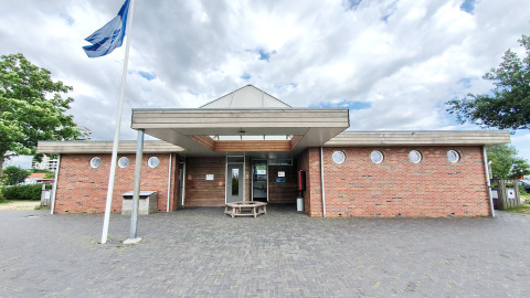 Ingang van een modern bakstenen gebouw met ronde ramen en vlag bij een glamping accommodatie.