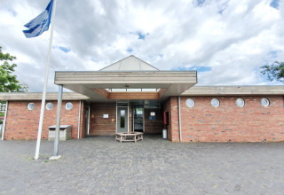 Ingang van een modern bakstenen gebouw met ronde ramen en vlag bij een glamping accommodatie.