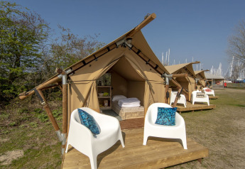 Tienda safari en Marina Parcs Almere, Países Bajos, con sillas blancas y cojines azules en terraza.