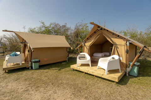 Safari tent with outdoor wooden deck and white chairs at Marina Parcs Almere, Netherlands, under blue sky.