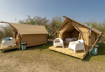 Safari tent with outdoor wooden deck and white chairs at Marina Parcs Almere, Netherlands, under blue sky.