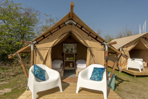 Safari tent at Marina Parcs Almere in the Netherlands with two white chairs and blue pillows on a wooden deck.
