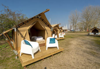 Tienda safari en Marina Parcs Almere, Países Bajos, con plataforma de madera, sillas y cielo soleado.